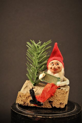 Fin lille gammel spillemands nisse siddende på træstub lavet af piberensere , ansigt i bemalet gips og nissehue i filt.H:11cm.