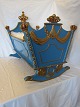 Vugge af blåmalet og delvist forgyldt træ. Oprindeligt tiltænkt prinsesse Anne-Marie af Danmark, søster til hendes Majestæt Dronning Margrethe II af Danmark.Udført i 1946 H: 75cm, L: 85cm, D: 55cm