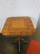 SkakbordSkakbord af palisander med intarsia af birke- og nøddetræSøjle formentlig bejdset bøgetræ, fødder af nøddetræAlle dele er med intarsiaH: 74,5cm, bordplade: 60cm x 60cmBemærk: Revne i bordplade