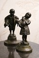 2 små dekorative bronze figurer af dreng med 2 grise under armen og pige der holder en gås...