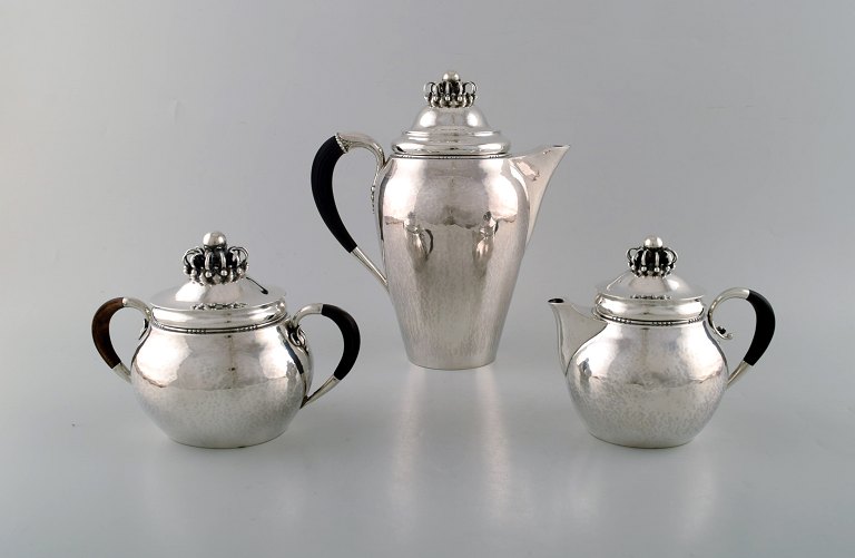 Sjældent Georg Jensen kaffeservice i sterlingsølv med hanke af ibenholt. Kaffekande, sukkerskål og flødekande. Låg udformet som kongekrone. Dateret 1915-30.