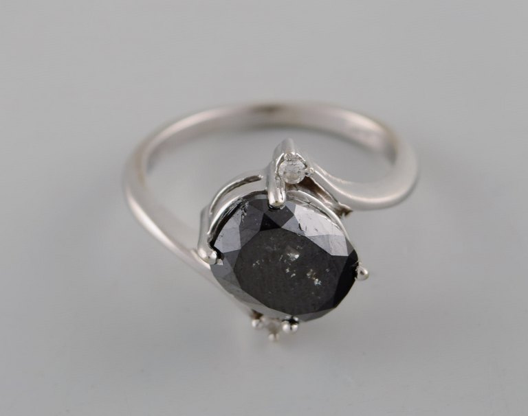 Large cocktail ring in 14 carat white gold with oval facet cut black diamond of approx. 3.50 ct. flanked by two brilliant-cut diamonds. Mid 20th century.