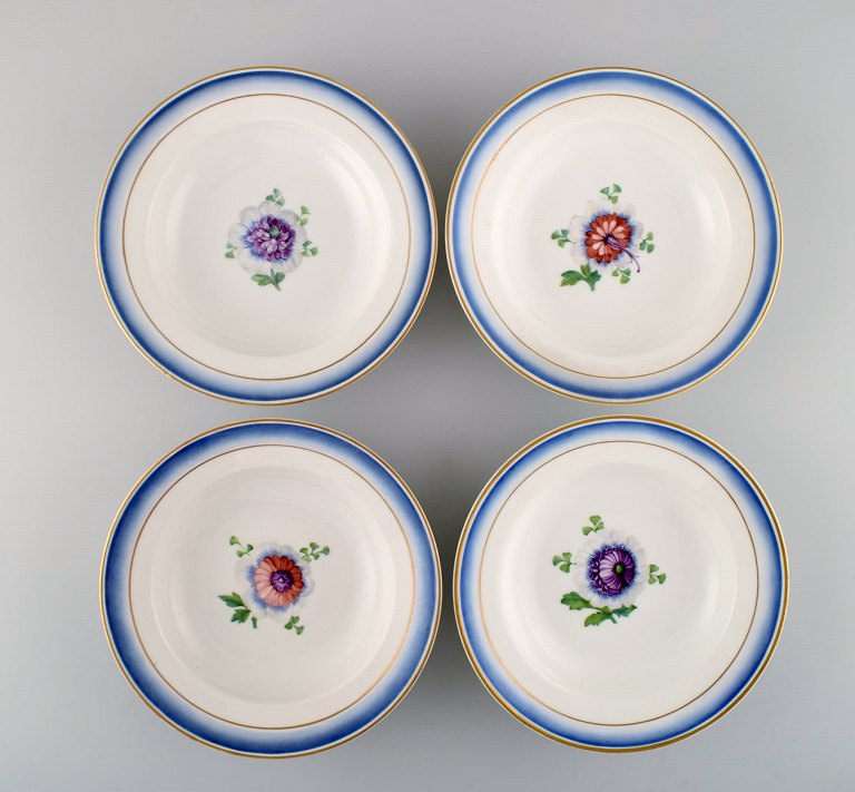 Four antique Royal Copenhagen deep plates in hand-painted porcelain with flowers and blue edge with gold. Model number 592/9050. Late 19th century.