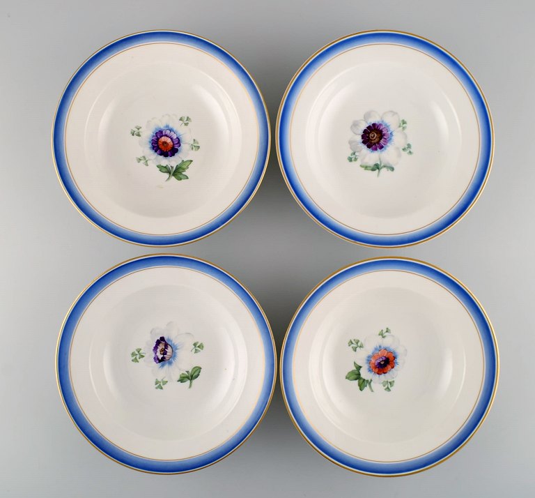 Four antique Royal Copenhagen deep plates in hand-painted porcelain with flowers and blue edge with gold. Model number 592/9049. Late 19th century.