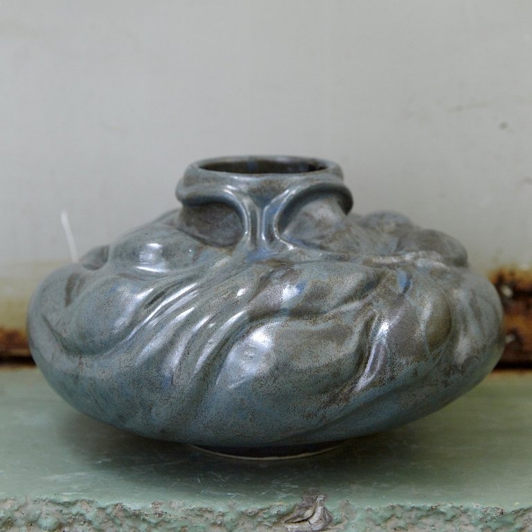 Christina Muff, dansk samtidskeramiker (f. 1971). Skulpturel vase dekoreret med spirende vækster. Denne unikavase er glaseret medsilkemat stålblå glasur der bryder i brunlige toner.