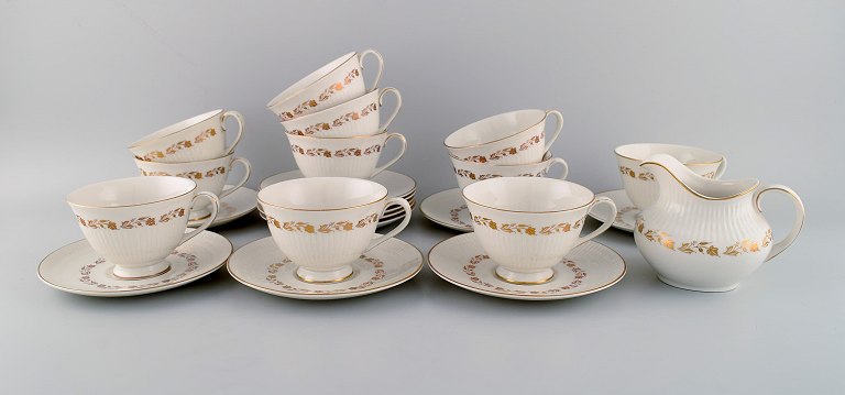Royal Doulton, England. Twelve Fairfax teacups with saucers and a cream jug in porcelain with hand-painted flowers in gold. Mid-20th century.