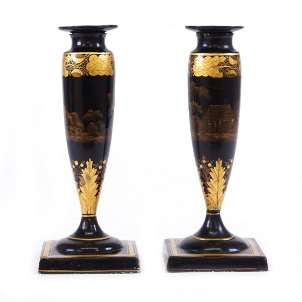 Et par sortlakerede lysestager dekoreret med forgyldte motiver i form af landskaber og stiliseret bladværk. England ca. år 1840. H: 19,5cm