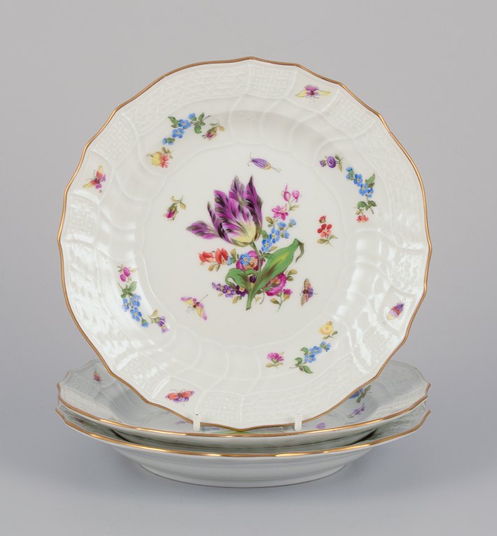 Meissen, Germany. Three plates in porcelain, hand-painted with different polychrome flowers and butterflies, and a gold rim.