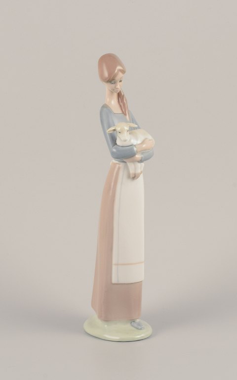 Lladro, Spain. Porcelain figurine of a standing young woman holding a lamb in her arms.