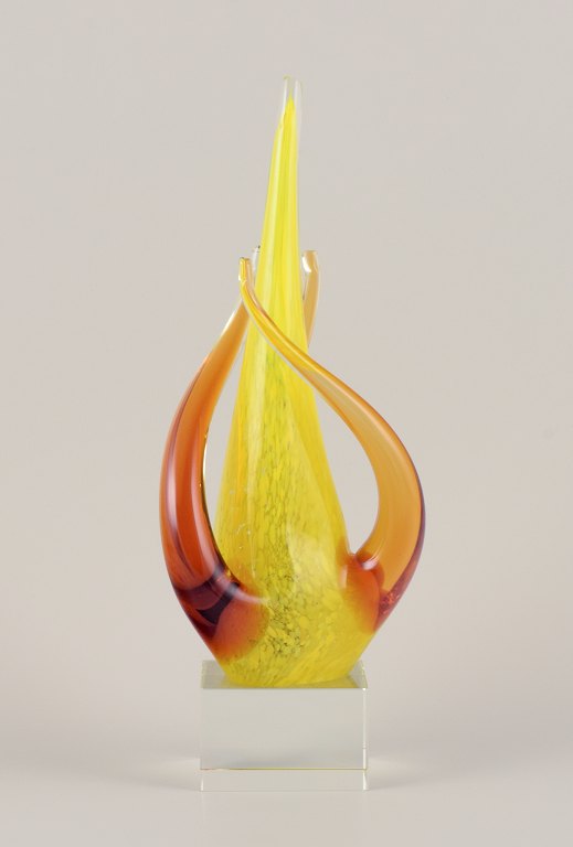 Swedish glass artist. Large sculpture in art glass.Yellow and amber decoration on a square base in clear glass. Mouth-blown.