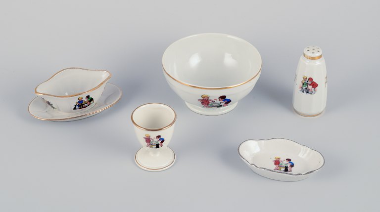 French childrens porcelain dinnerware consisting of a bowl, egg cup, pepper shaker, miniature sauce boat, and a small oval dish. Motifs of children at play.