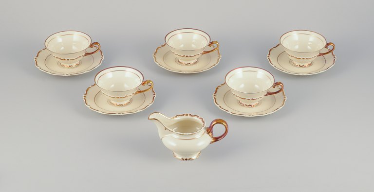 Et sæt på fem KP, Karlskrona tekopper med underkopper samt flødekande i cremefarvet porcelæn med gulddekoration.
