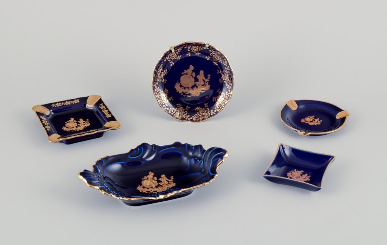 Limoges, France. Five pieces of porcelain including small trays and bowls, decorated with 22-karat gold leaf and a beautiful royal blue glaze. Scène galante.