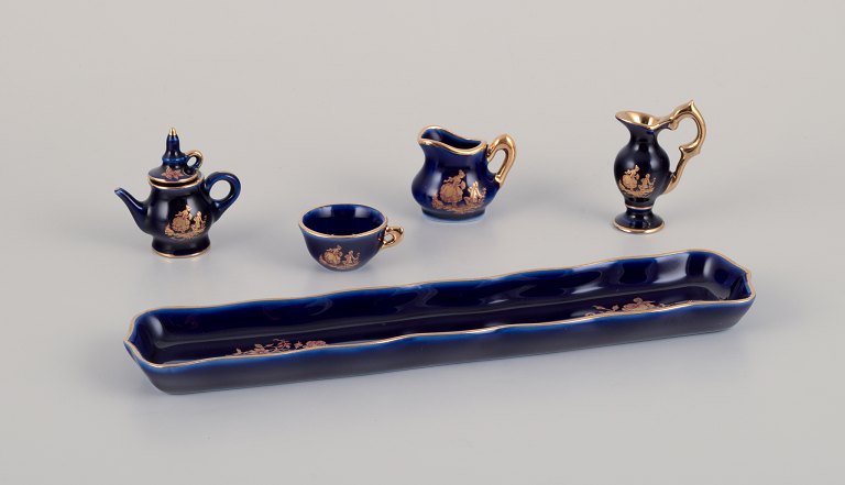 Limoges, Frankrig. Miniatureporcelæn bestående af kop, tekande, to kander samt bakke. Dekoreret i 22-karat bladguld og smuk kongeblå glasur. Scène galante.