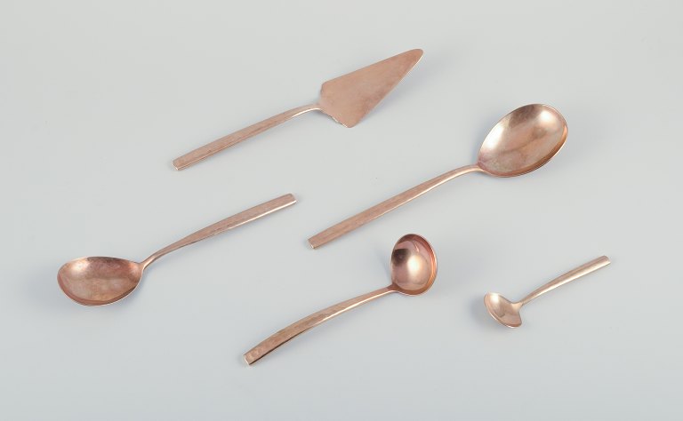 Skandinavisk designer. Fem serveringsdele bestående af sauceske, to store serveringsskeer, marmeladeske samt en smørrebrødsspade i hammerslået messing. Håndlavet i høj kvalitet.